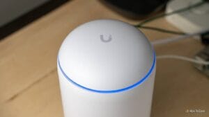 A white cylindrical networking device with a glowing blue LED ring on top, placed on a wooden surface.